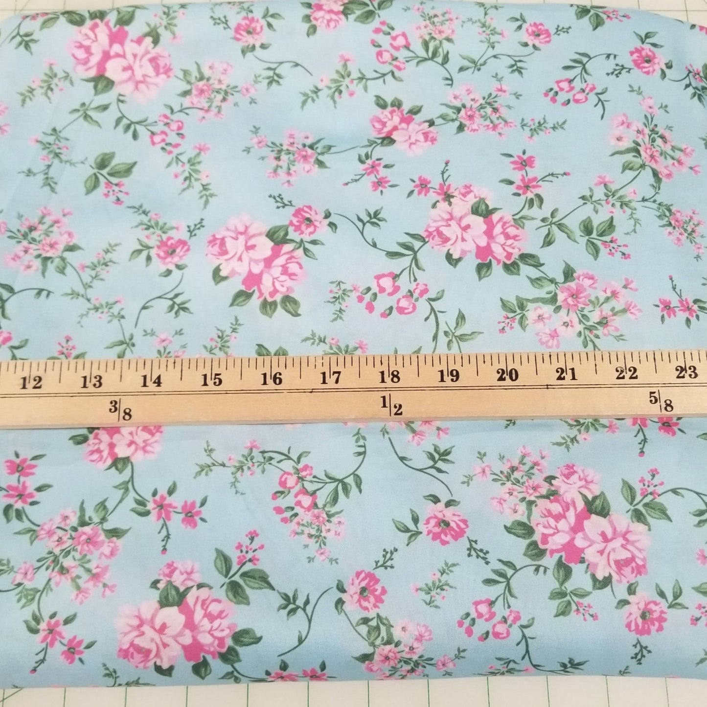 Floral fabric with pink flowers on a blue background, measured with a ruler.