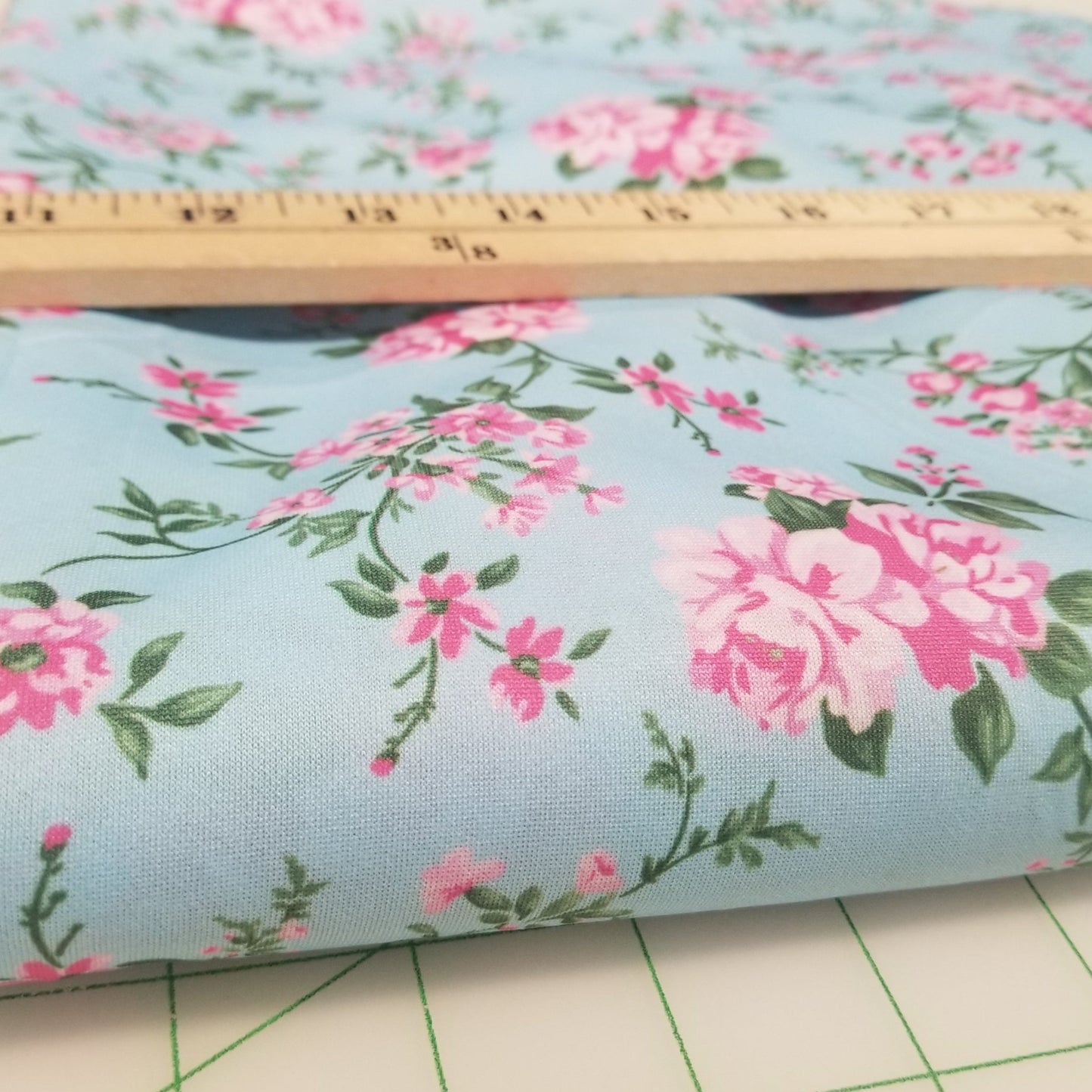 Floral fabric roll with pink flowers on a light blue background, next to a ruler and cutting mat.
