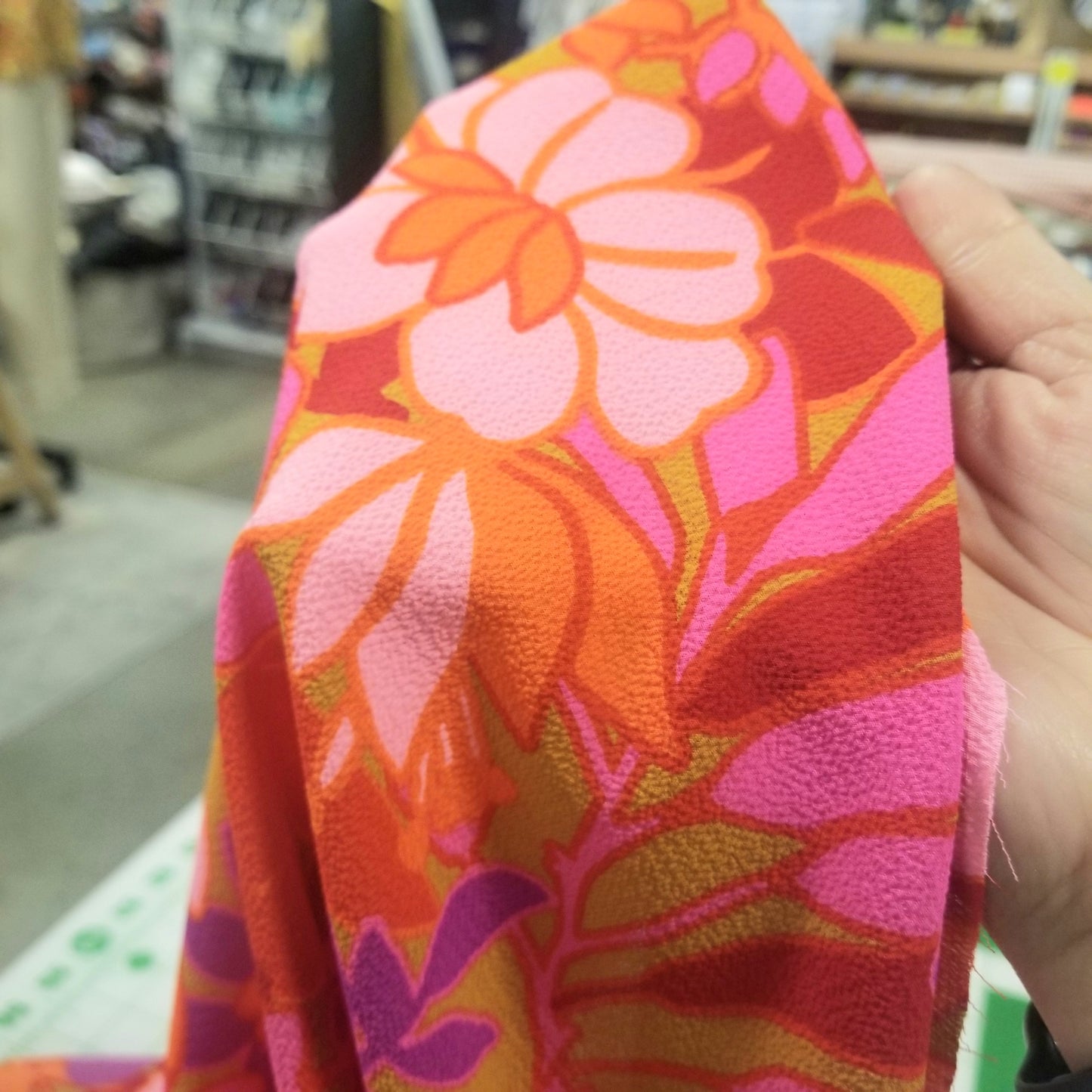 Hand holding a colorful floral fabric with a blurred store background