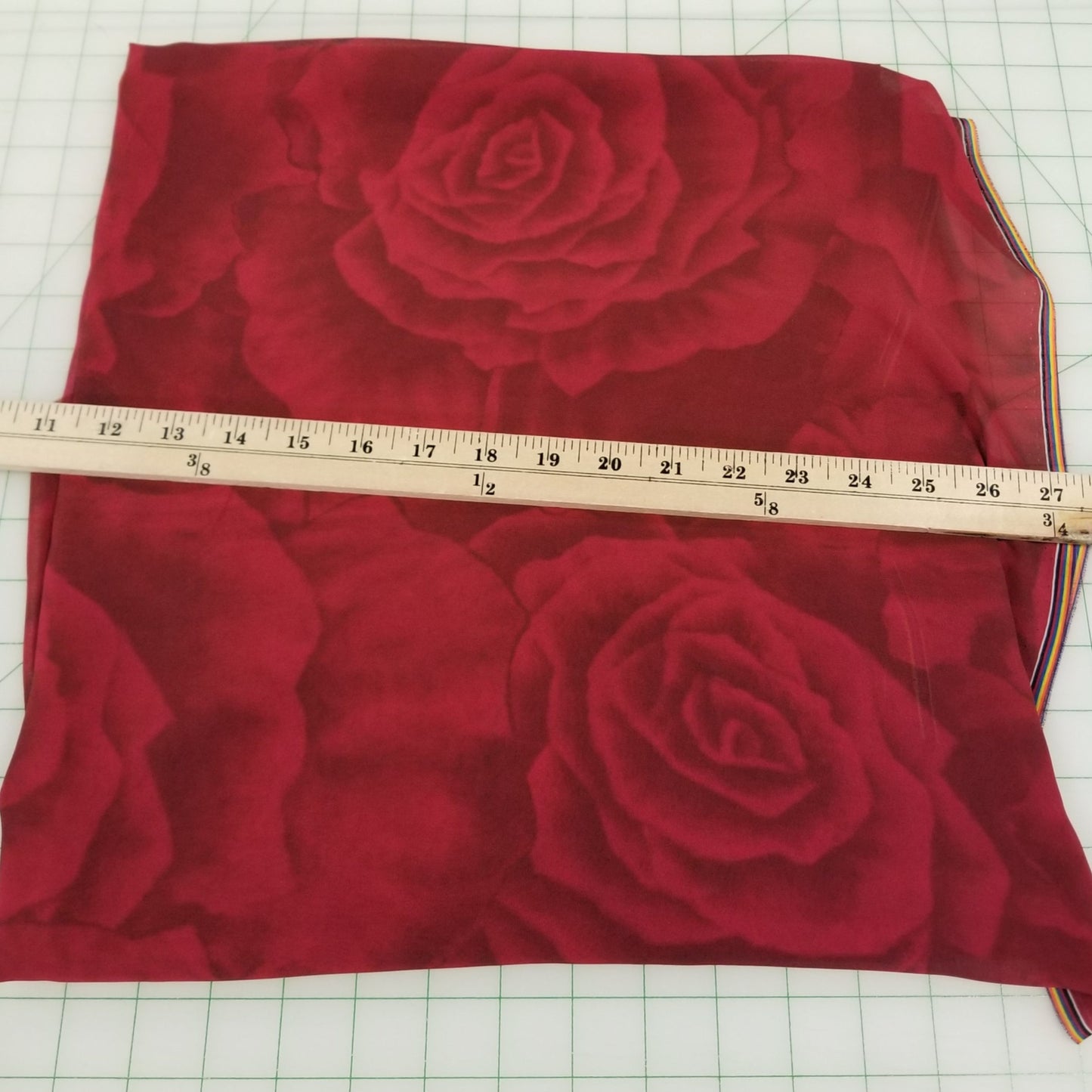 Red fabric with rose pattern on a grid background, measured with a ruler.