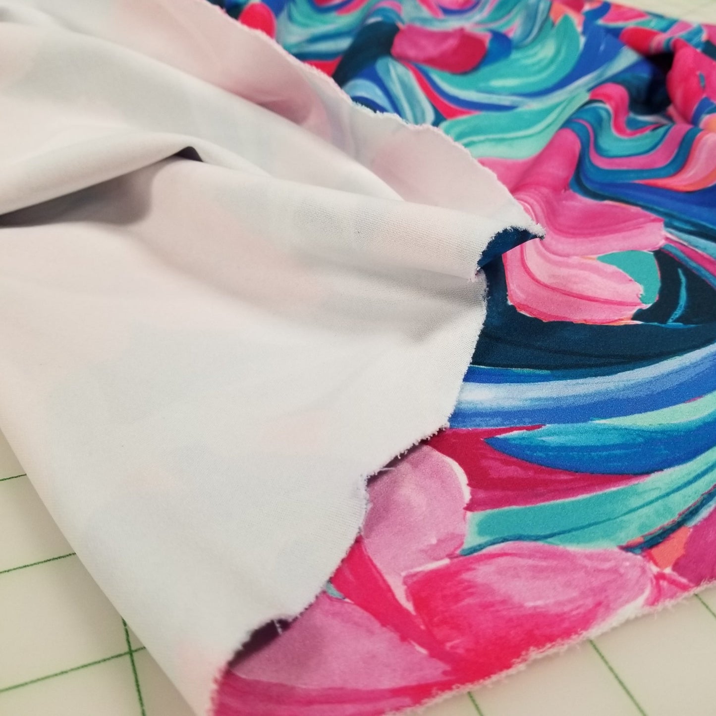 Close-up of colorful fabric with pink, blue, and green swirls on a white background.