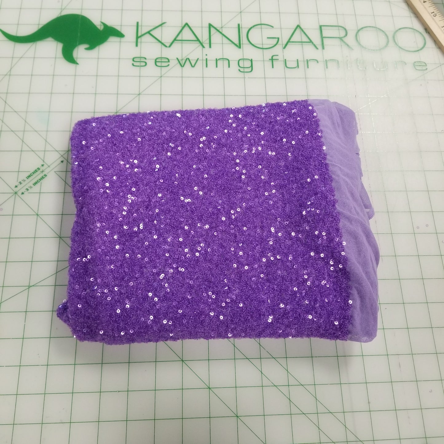 Purple sequined fabric on a green cutting mat with Kangaroo Sewing Furniture logo.