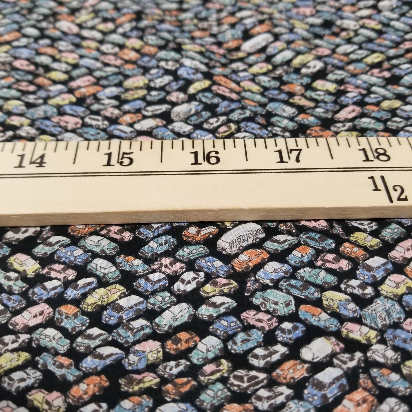 Close-up of a fabric with a pattern of small, multicolored shapes on a black background, with a ruler for scale.