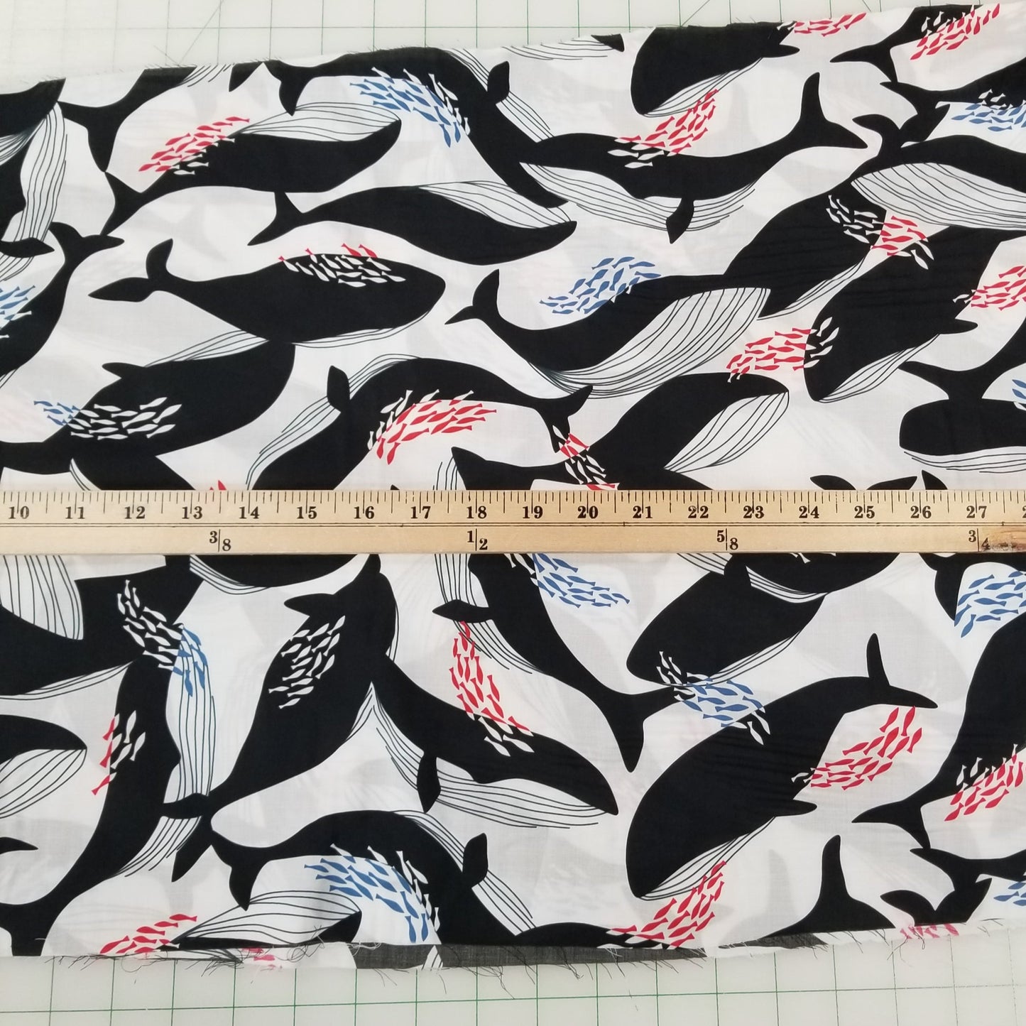 Fabric with black whale pattern on a white background, measured by a ruler.