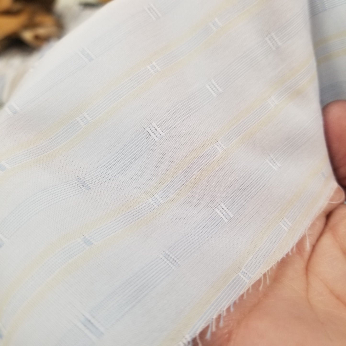 Close-up of a textured white fabric with subtle patterns held by a hand.
