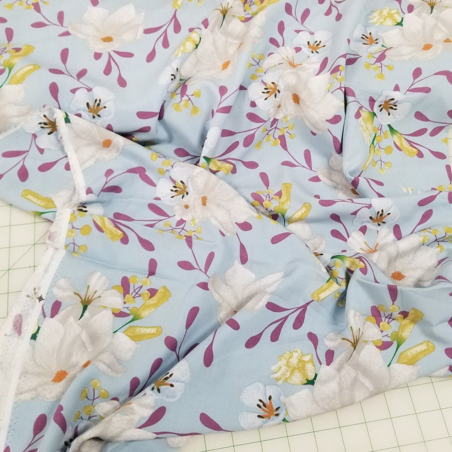 Floral fabric with white flowers and colorful leaves on a light blue background, laid out on a grid surface.