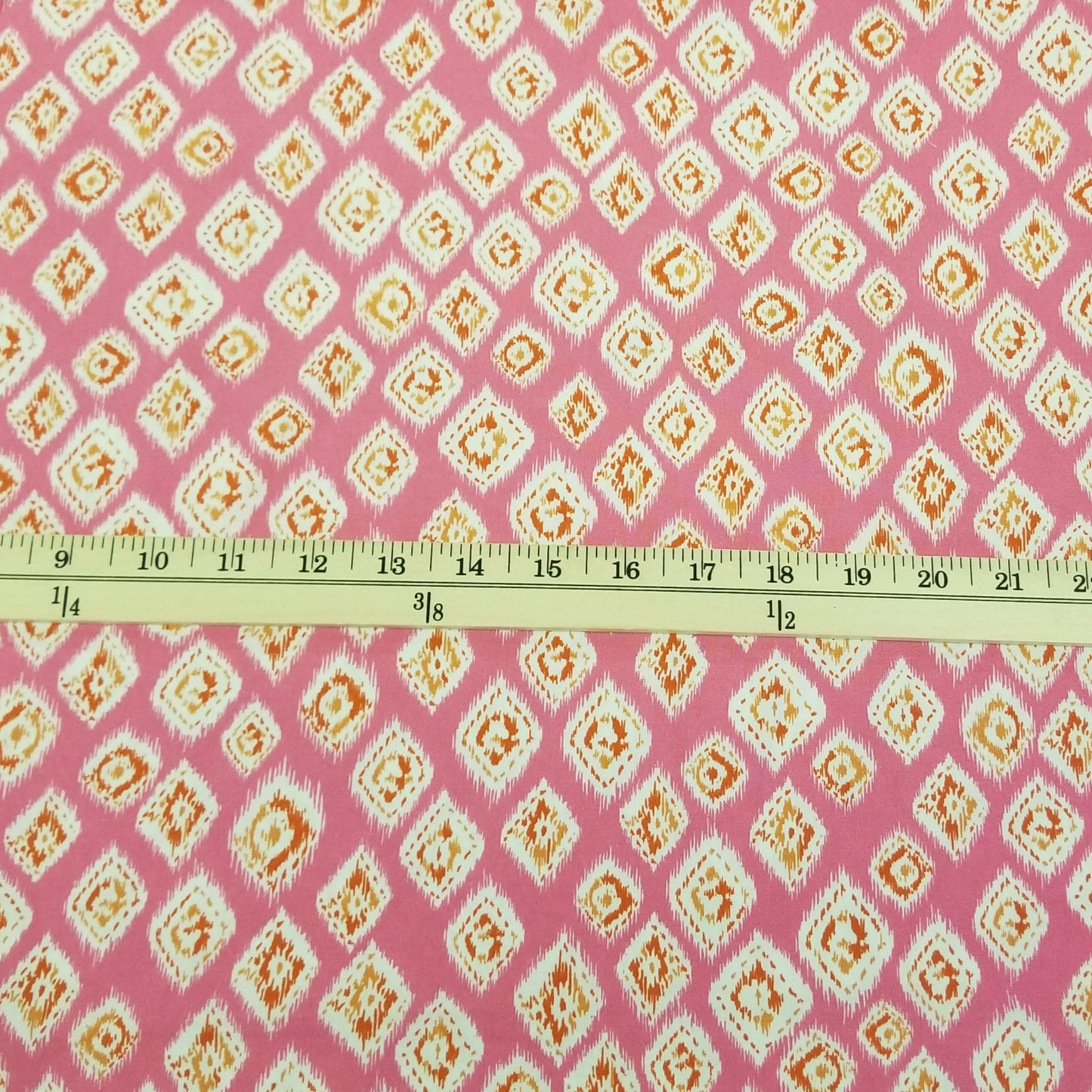 Fabric with a diamond pattern on a pink background, measured by a ruler.