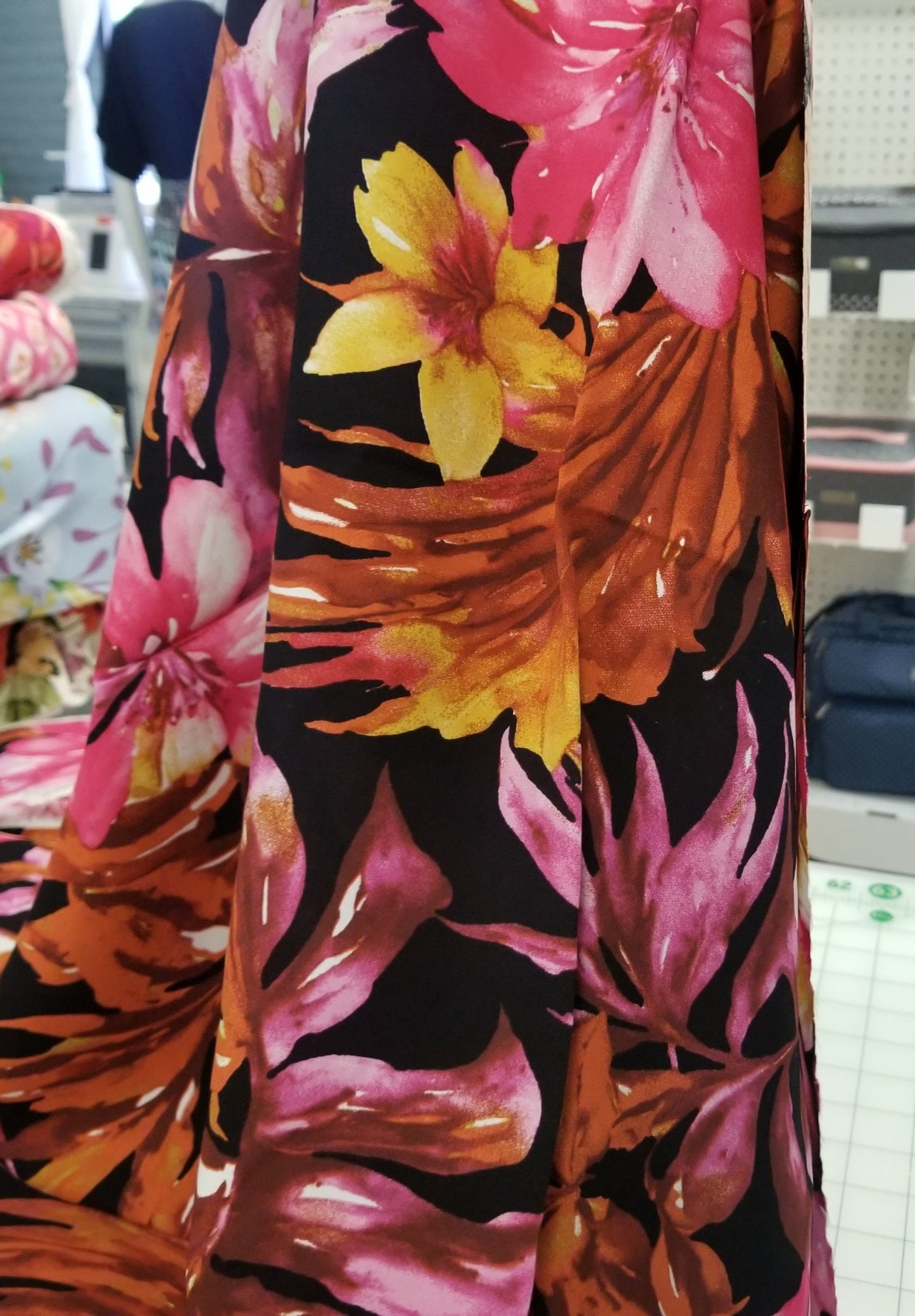 Floral fabric with pink, yellow, and orange flowers on a black background, displayed in a store setting.