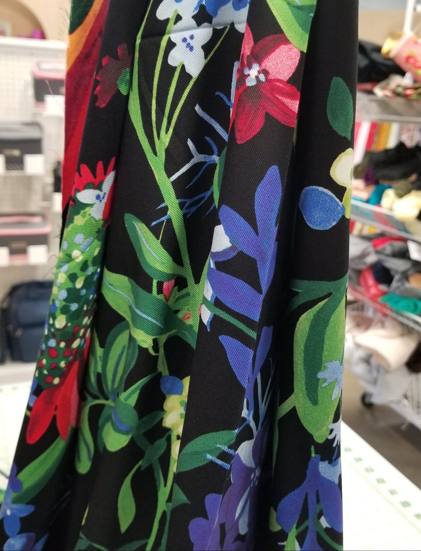 Colorful floral pattern on black fabric with a blurred store background