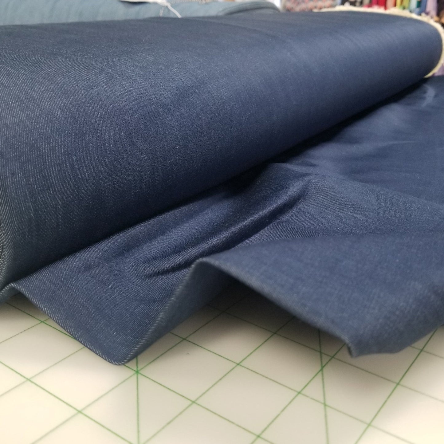 Roll of blue fabric on a cutting mat with a store setting in the background