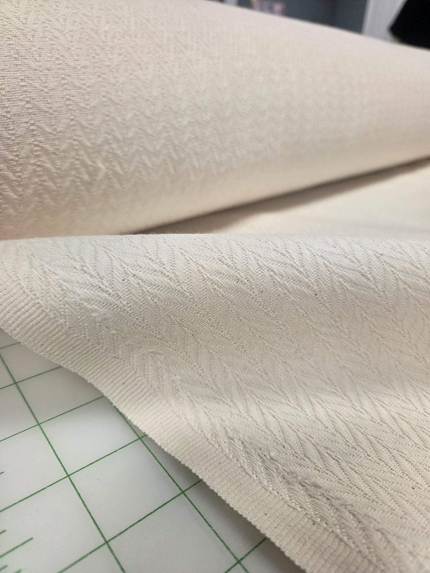 Close-up of textured beige fabric on a grid background.chevron woven for garment making