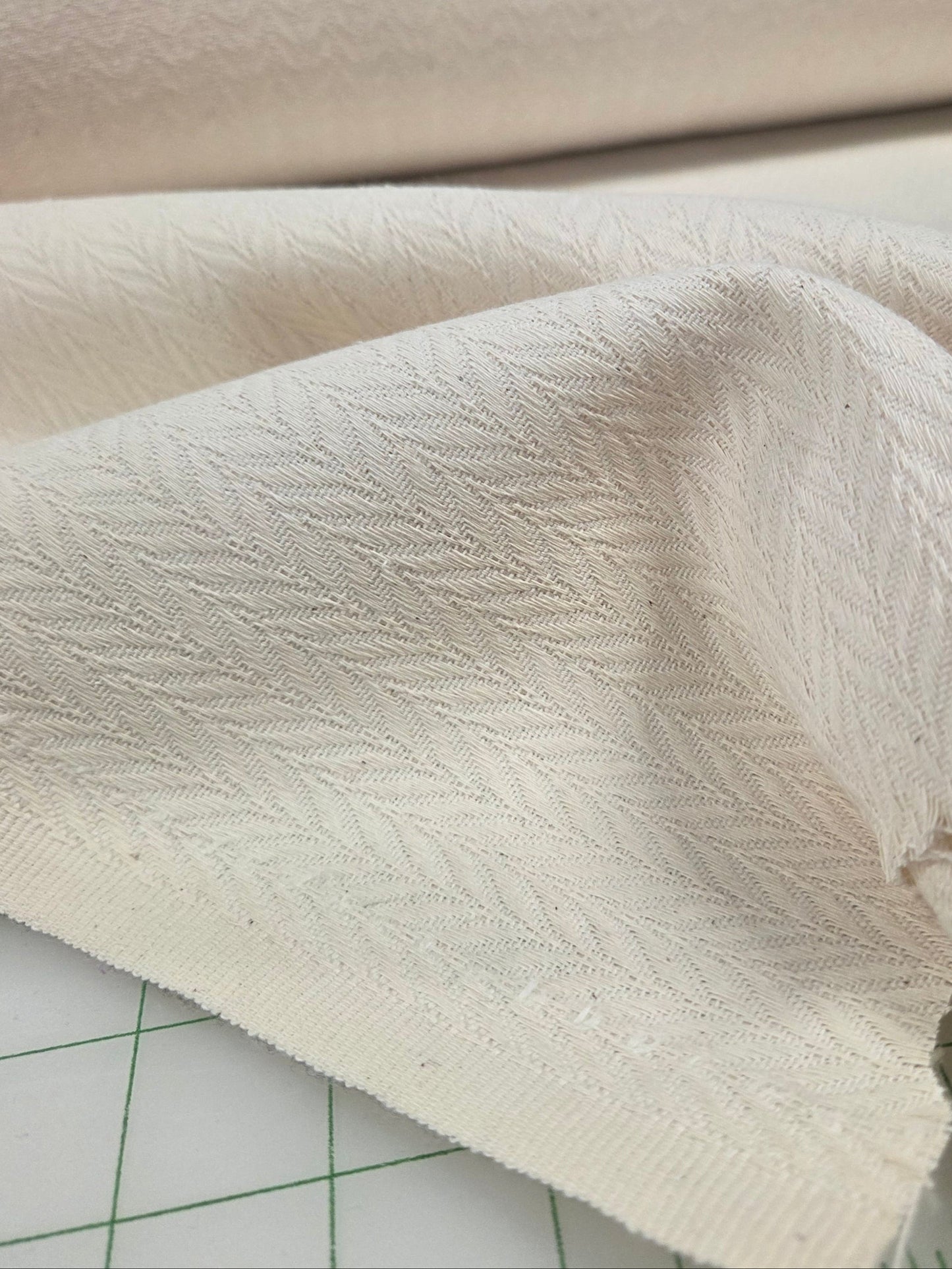 Close-up of textured cream herringbone fabric on a cutting mat with ruler