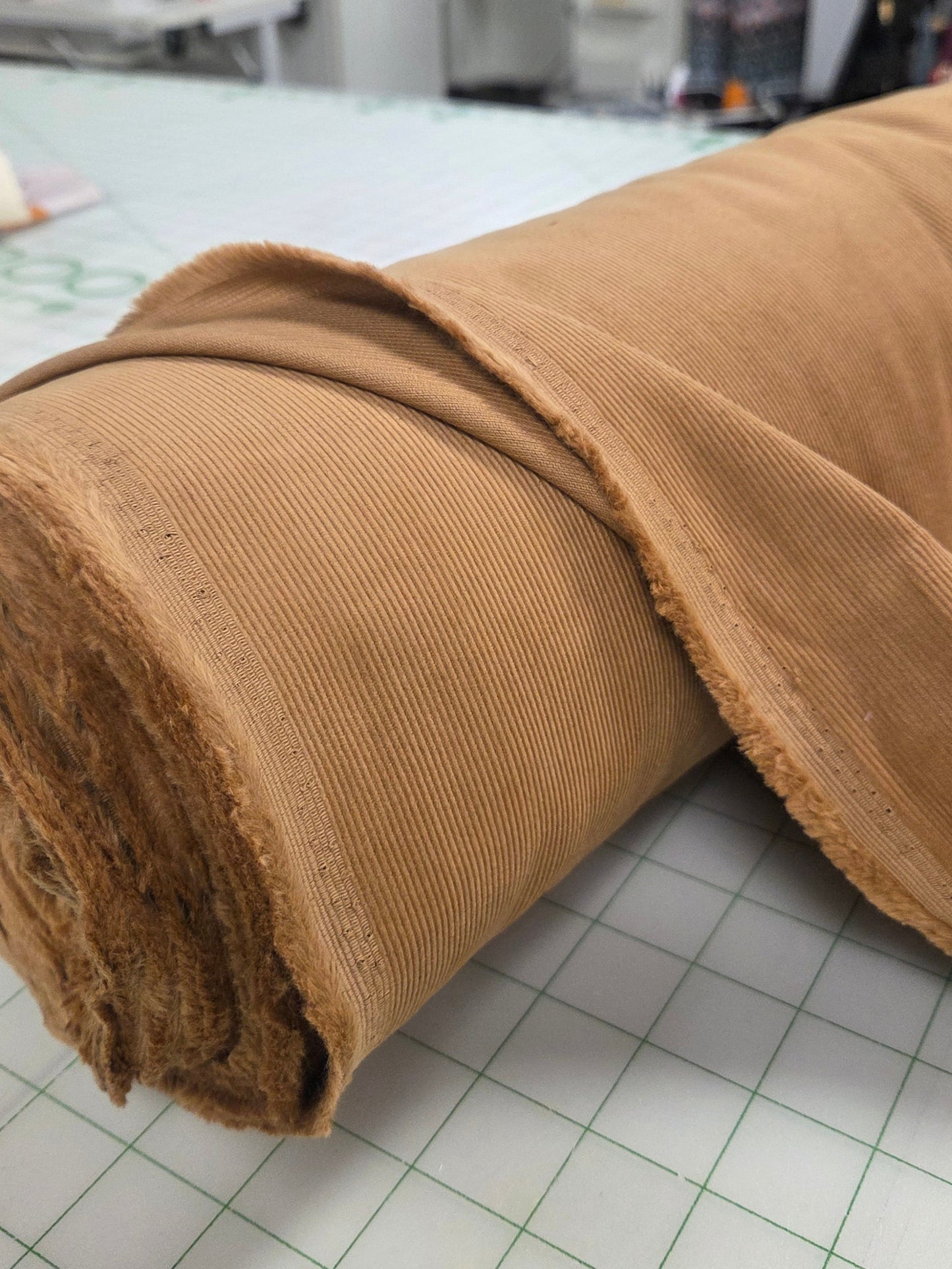 Roll of brown fabric on a grid surface with a store background. camel cotton corduroy. LA Finch Fabric by the yard