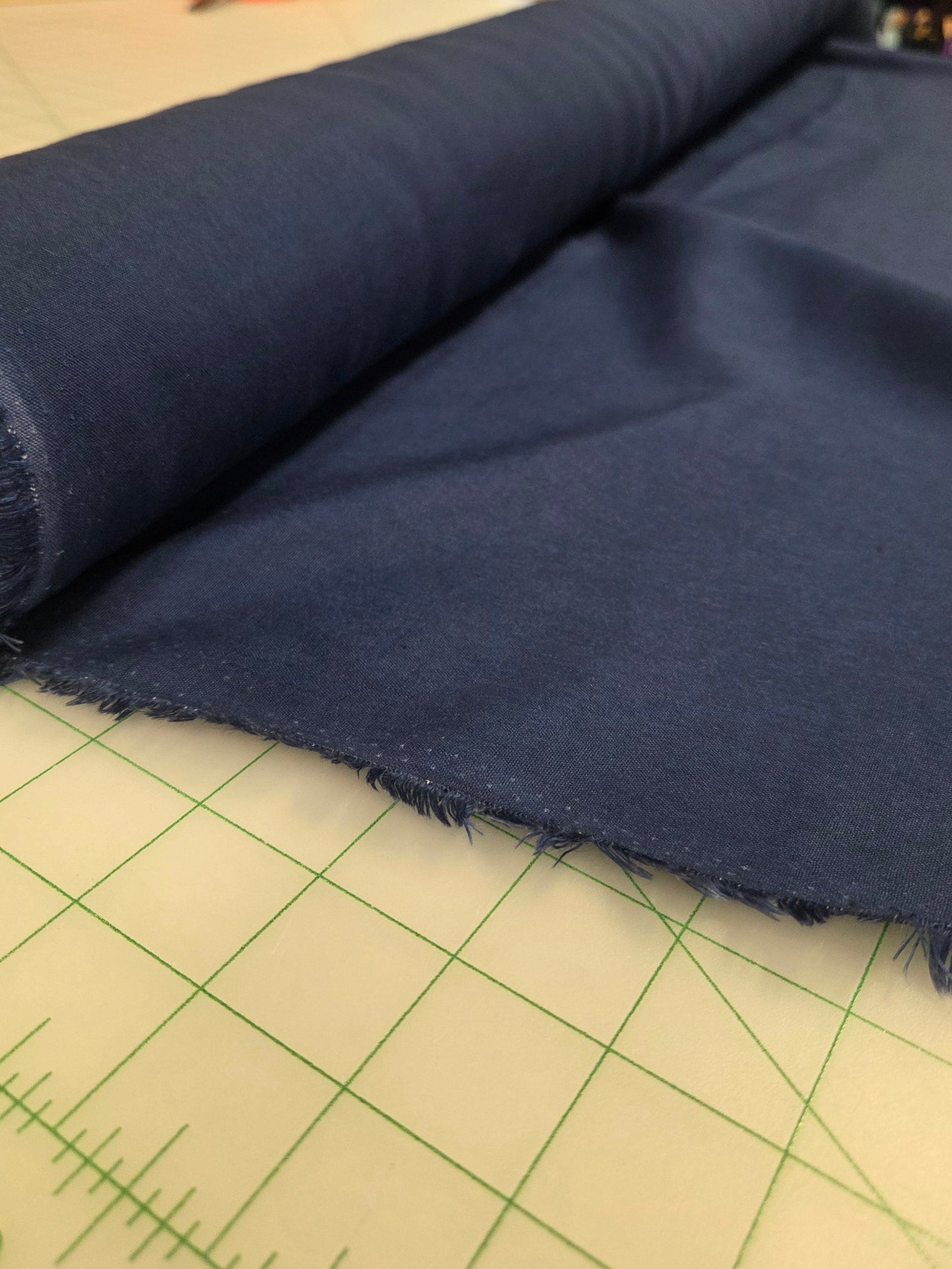 Roll of blue fabric on a cutting mat with a store background. Laundered linen by the yard