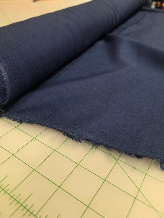 Roll of blue fabric on a cutting mat with a store background. Laundered linen by the yard