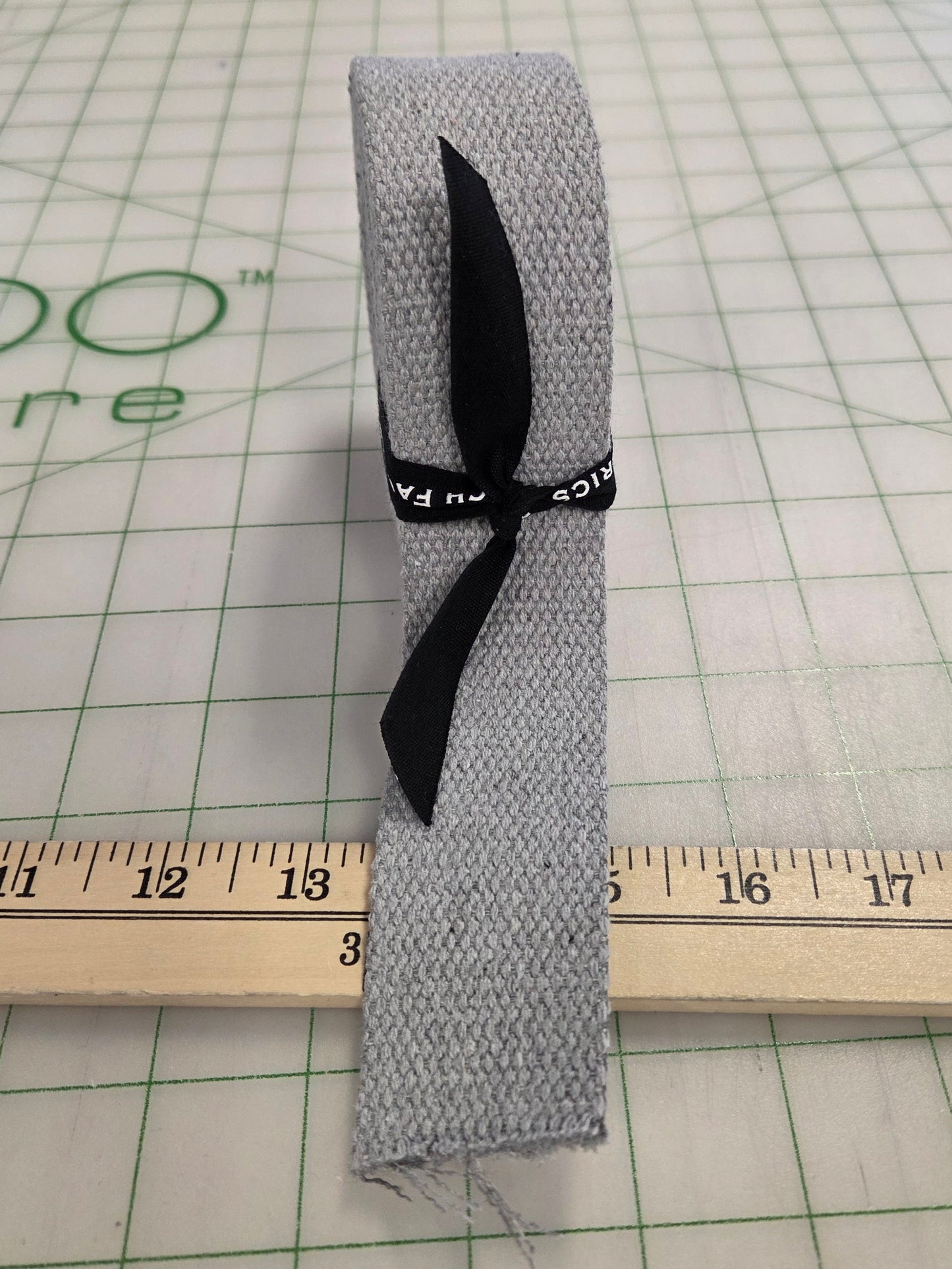 Gray fabric strip with a black ribbon on a grid background with a ruler.