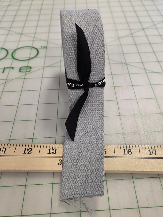 Gray fabric strip with a black ribbon on a grid background with a ruler.