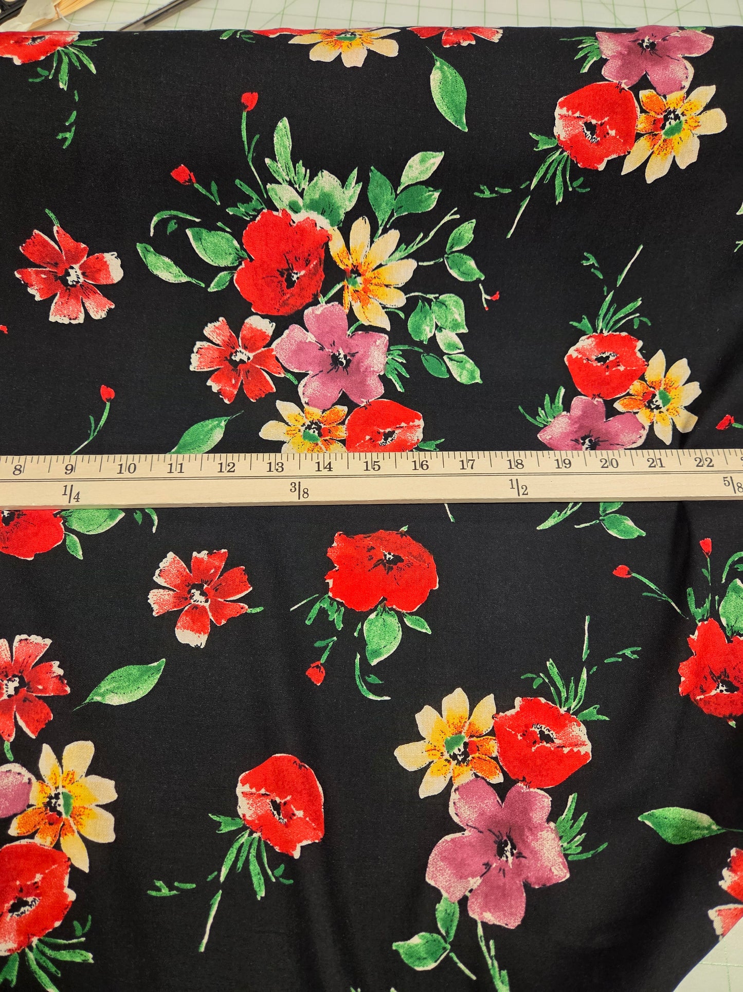 Floral fabric with red, yellow, and pink flowers on a black background, measured with a ruler.
