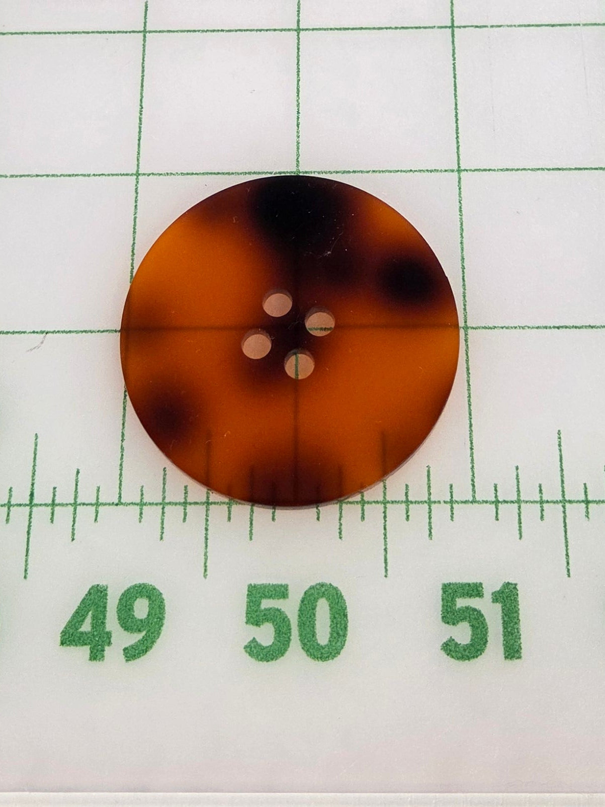 Two tortoiseshell buttons on a grid background with a ruler for scale.