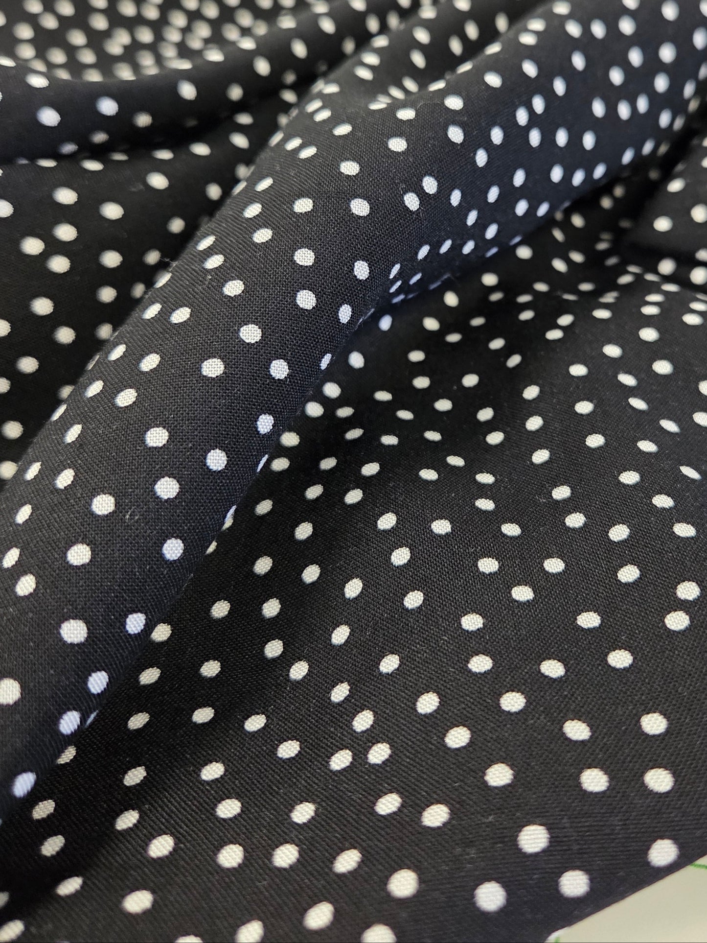 Black fabric with white polka dot pattern on a green grid background