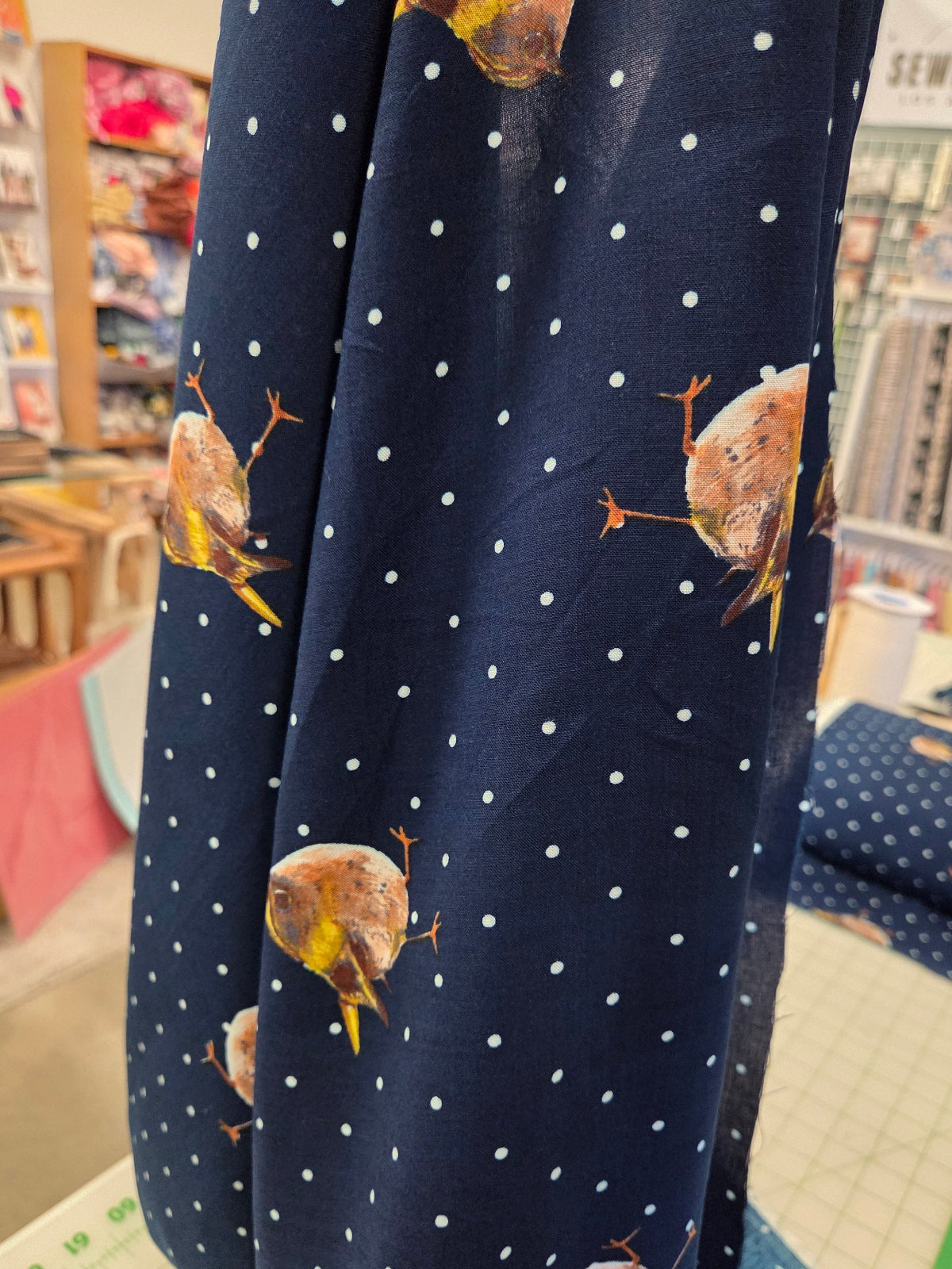 Navy fabric with white polka dots and bird patterns, held up indoors.
