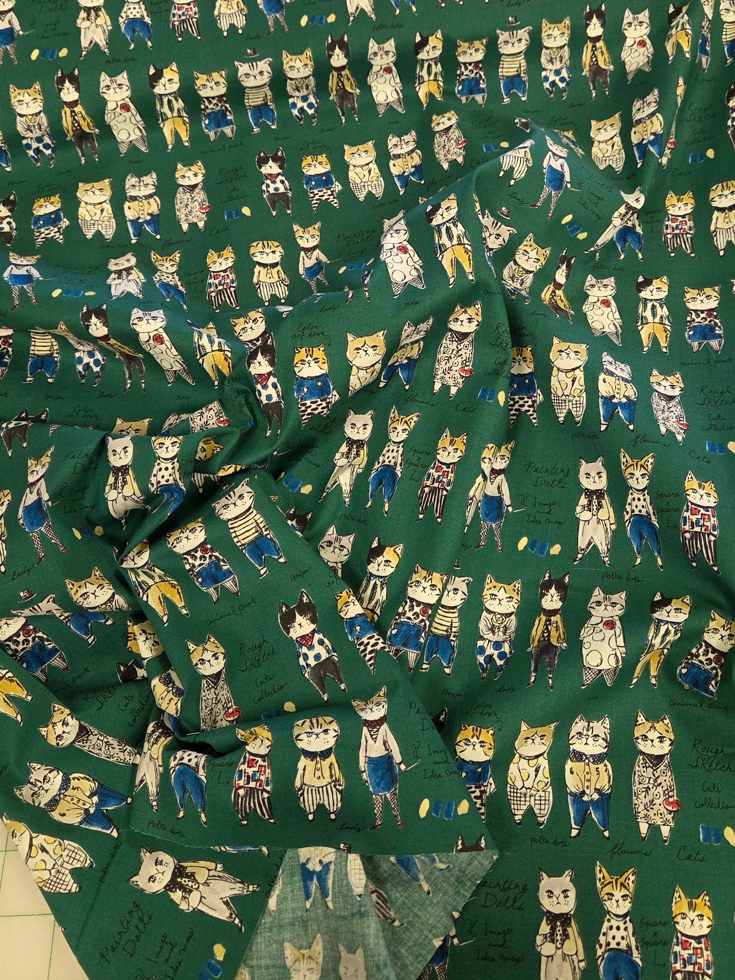 A piece of dark green fabric with a repeating pattern of cartoon owls in blue, white, and beige, laid out on a white gridded cutting mat.