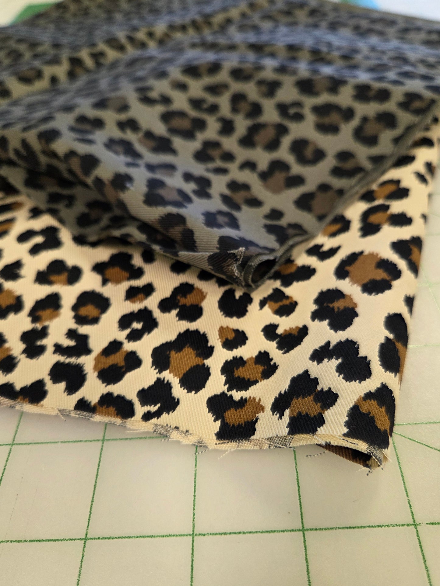 Leopard print fabric draped over a white gridded cutting mat, showing a black, brown, and beige animal spot pattern.