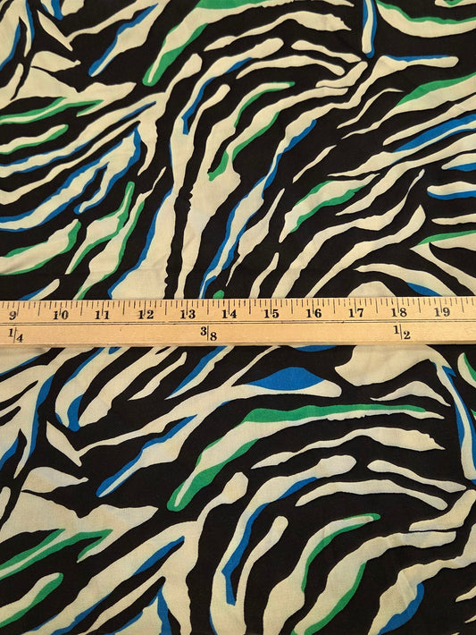 A folded piece of fabric with a zebra-stripe pattern in black, white, blue, and green, shown next to a wooden ruler on a green grid cutting mat.