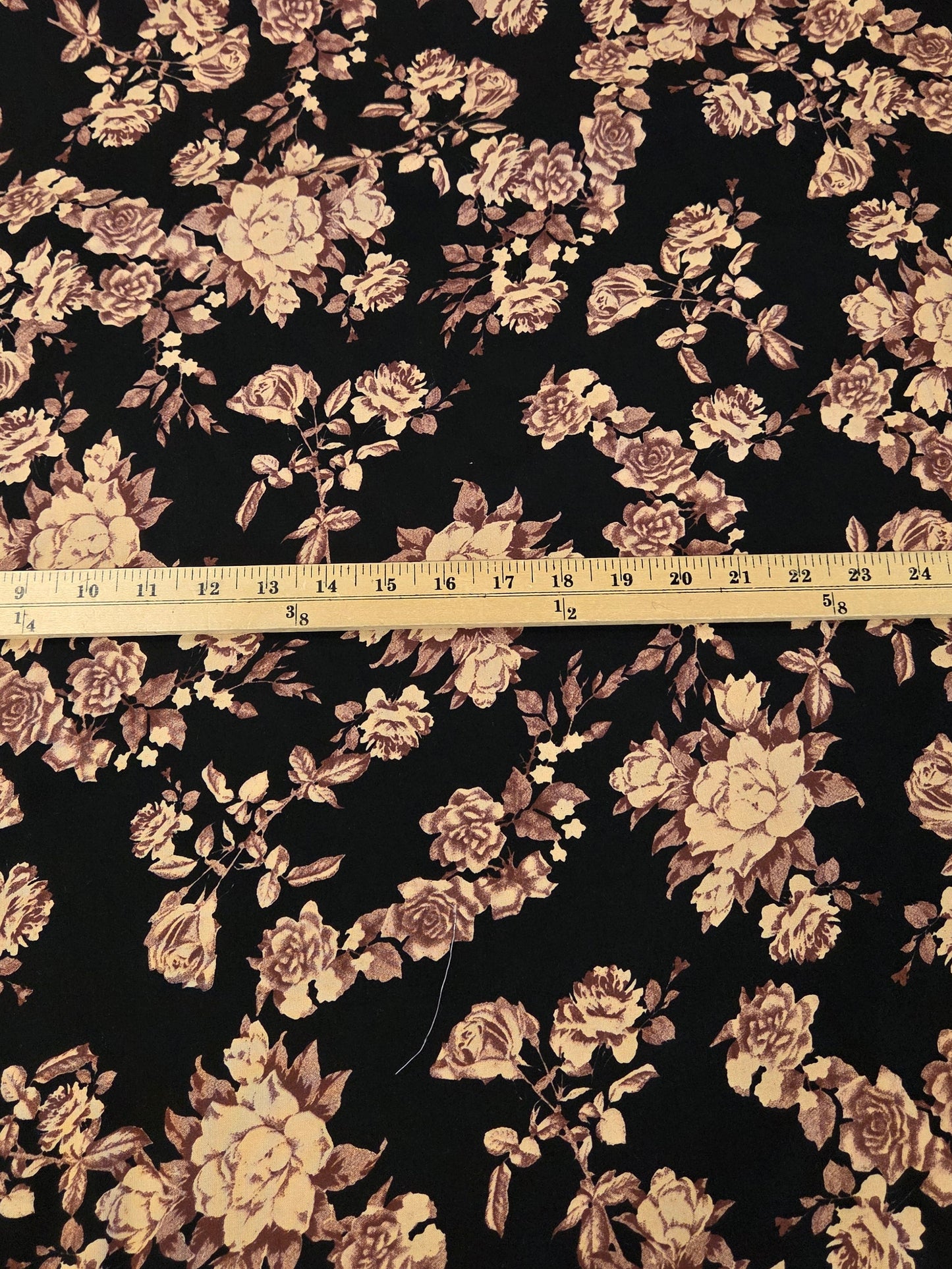 Black floral fabric with a vintage rose pattern in beige and brown, shown with a wooden ruler in the center for scale.