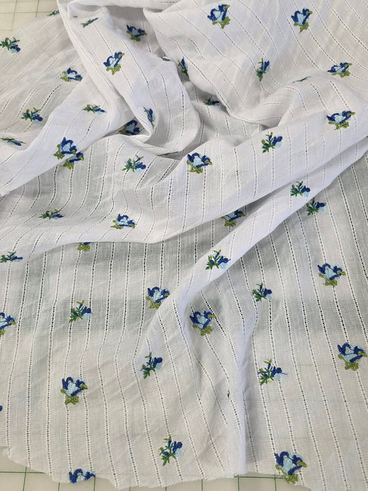 White muslin fabric with a delicate blue and green floral pattern, draped on a green grid cutting mat.