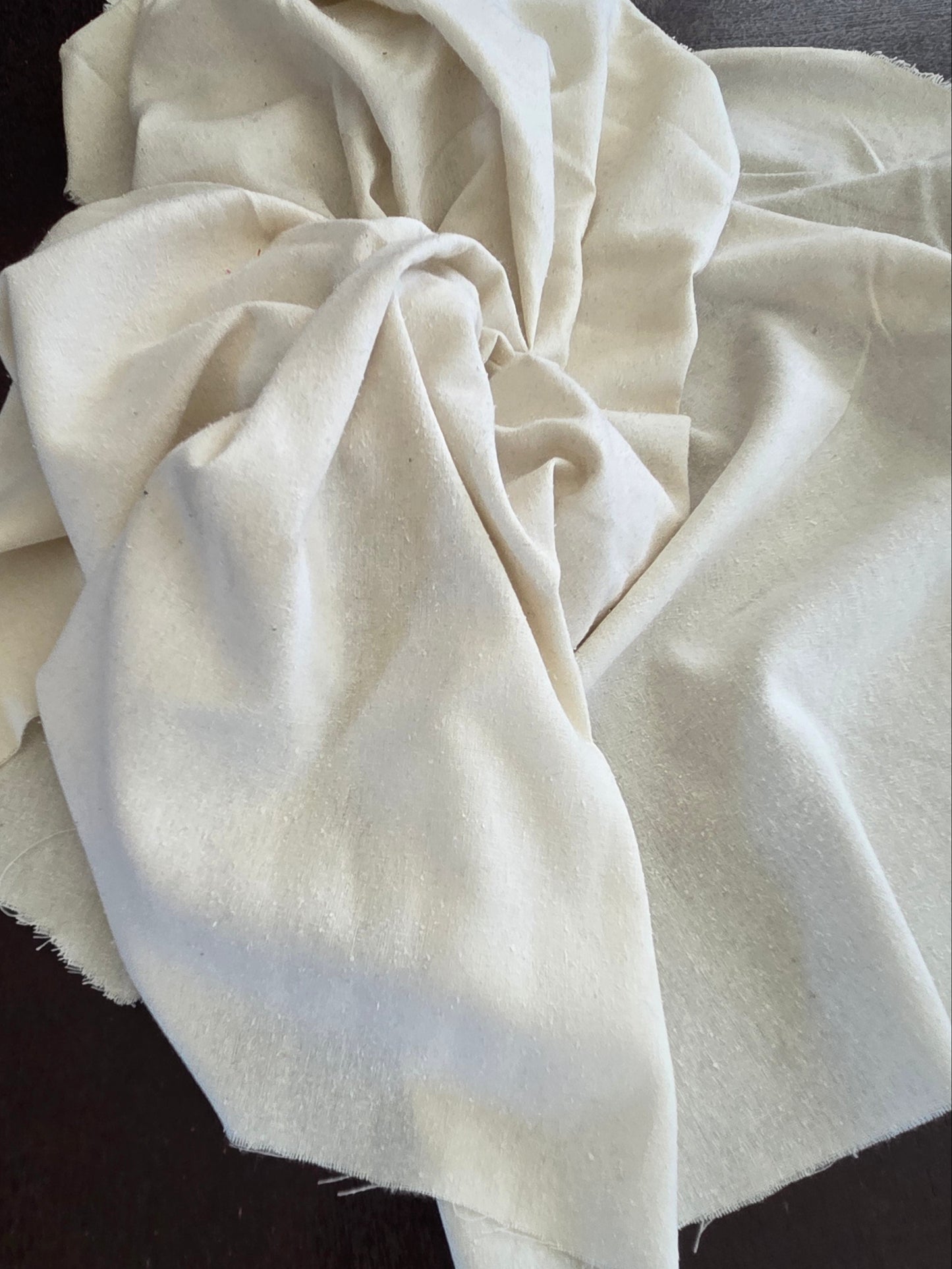 A draped piece of off-white cotton fabric with a soft, slightly textured surface, arranged on a dark wooden background.