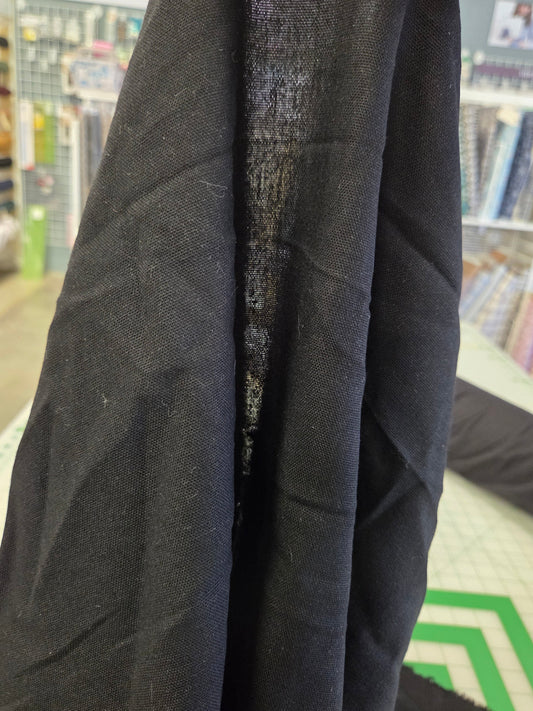 A close-up of a black linen fabric being held up in a sewing or fabric store, showing its texture and weave.