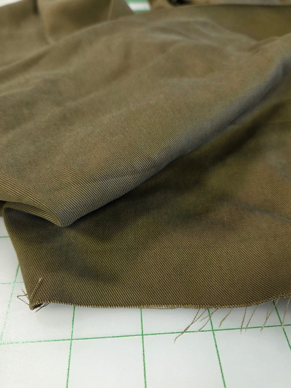 A close-up of olive green fabric draped over a white gridded cutting mat.