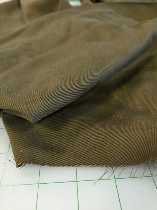A close-up of olive green fabric draped over a white gridded cutting mat.