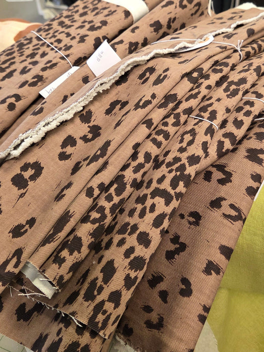 A stack of leopard print fabric bolts in a brown and black pattern, displayed on a table inside a fabric store.