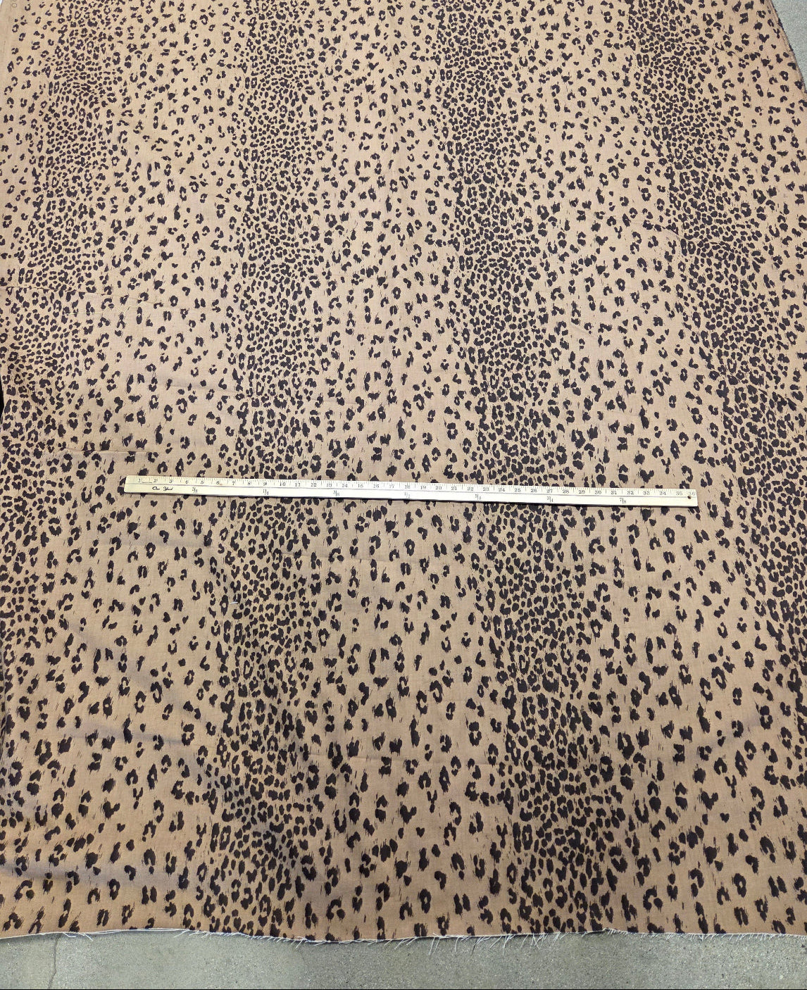 A large piece of leopard print fabric spread out on a floor, with a wooden ruler placed horizontally across the center for scale.