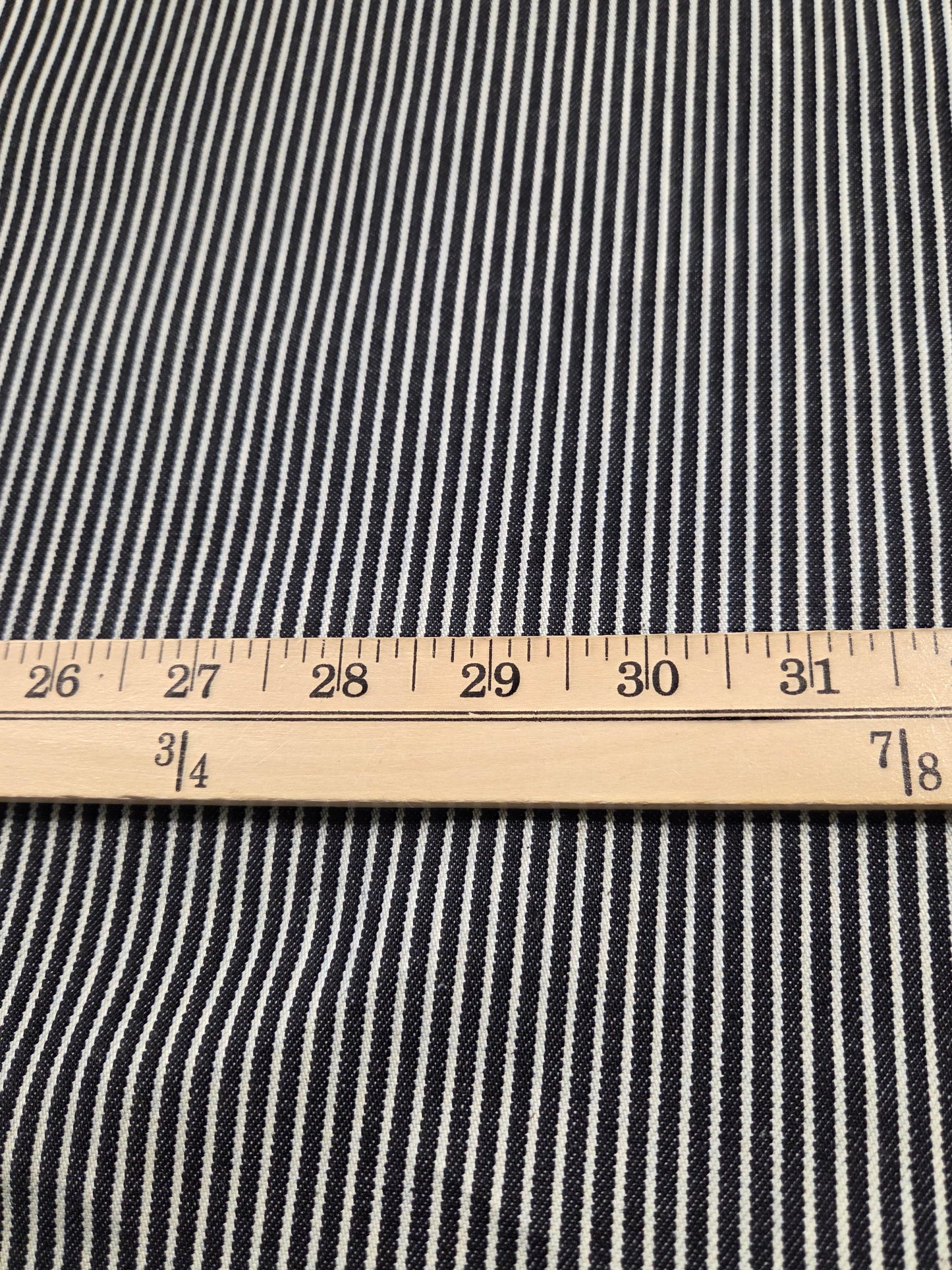 Close-up of a black and white striped fabric with a wooden ruler laid horizontally to show the scale of the pattern.