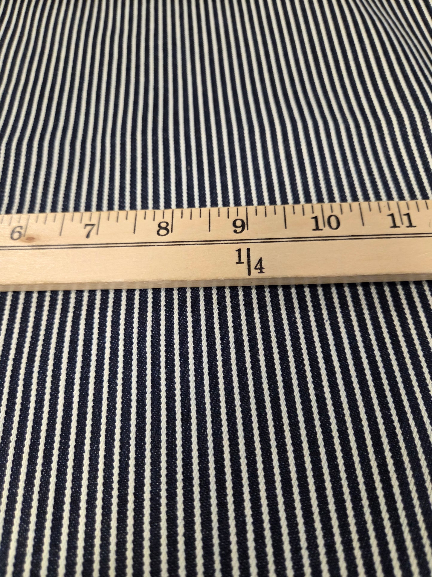 Close-up of a navy and white striped fabric with a wooden ruler placed horizontally to show the pattern scale.