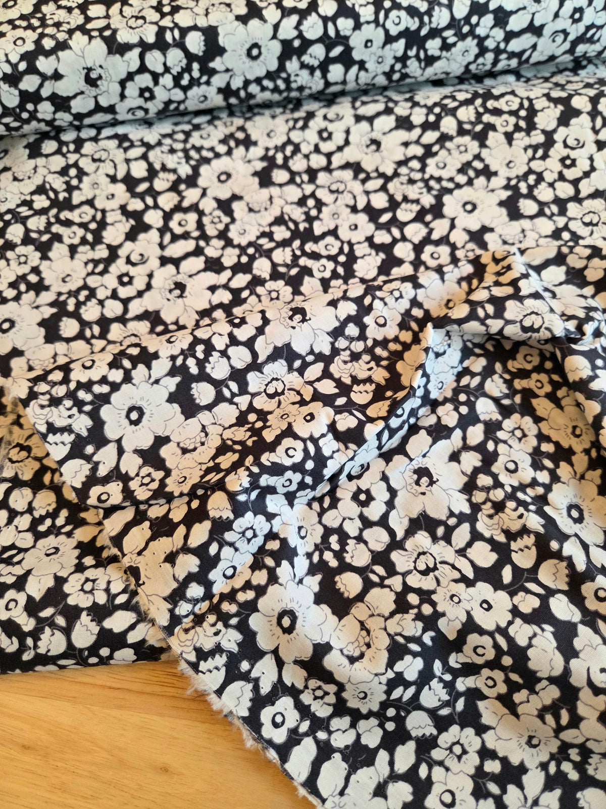 navy fabric with a dense white and beige floral print, draped to show its texture and pattern.