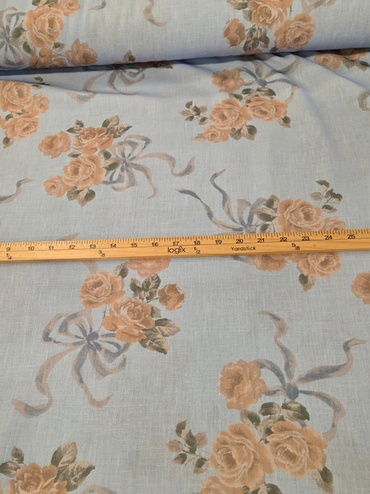 Light blue fabric with a floral rose pattern in peach and green, laid out with a wooden measuring tape ruler across the middle.