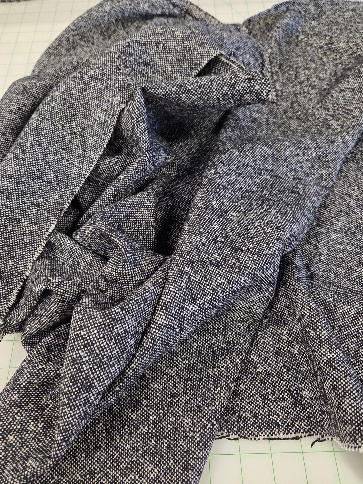 A close-up of dark heather gray fabric draped over a green grid cutting mat, with a matching folded piece of fabric visible along the top edge. italian wool blend tweed