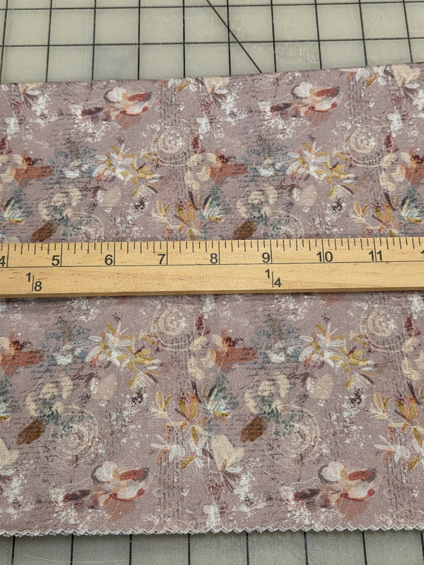 A piece of floral fabric with a dusty mauve background and a vintage-style print, shown next to a wooden ruler on a gridded cutting mat.