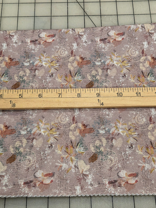 A piece of floral fabric with a dusty mauve background and a vintage-style print, shown next to a wooden ruler on a gridded cutting mat.