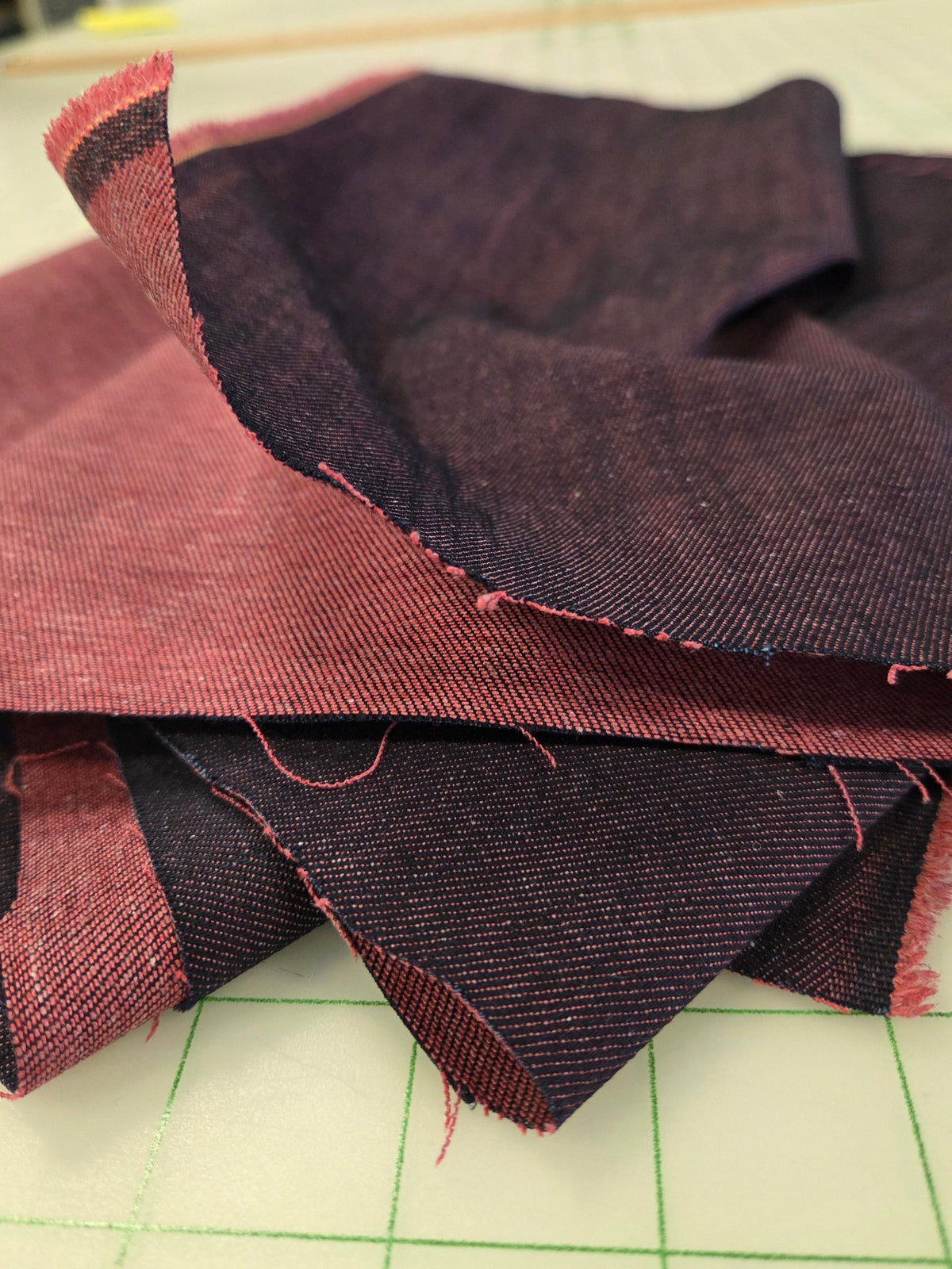 Dark charcoal gray and dusty rose fabric pieces layered together, showing raw woven texture and frayed edges, photographed against a light green grid cutting mat.