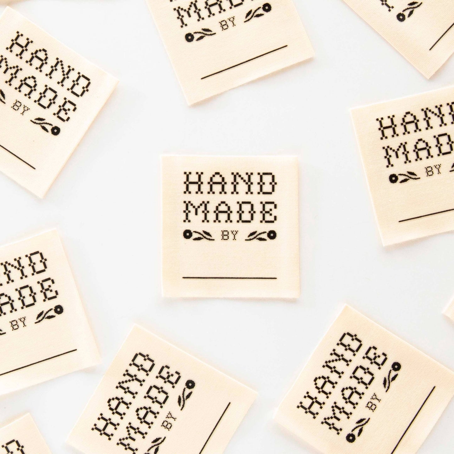 Multiple 'Hand Made by' labels scattered on a light background. Sarah hearts, La Finch Fabrics garment labels