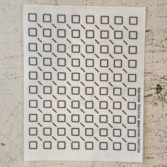 White cloth with black geometric pattern on a textured beige surface. mending supplies