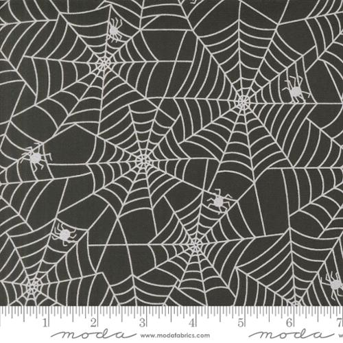 Fabric with spider web pattern on a black background, featuring Moda label.