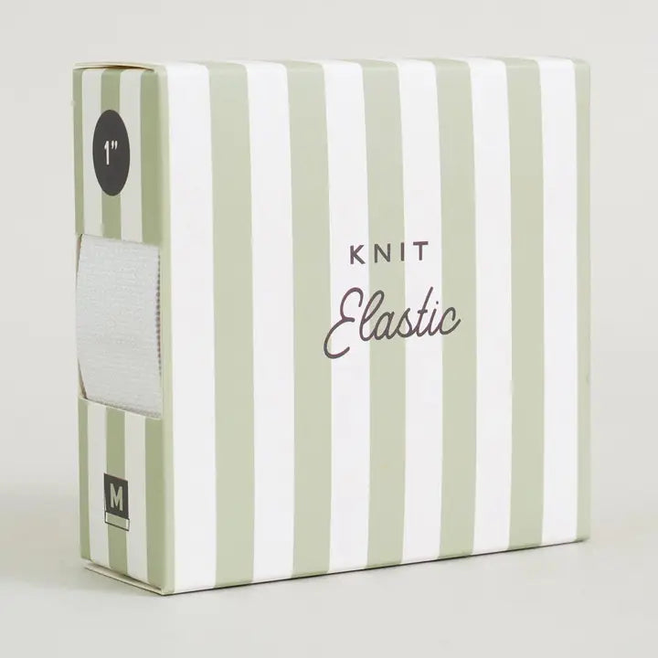A box of Knit Elastic yarn, featuring a white and sage green striped design. The front of the box displays the text 'KNIT Elastic' in black and gray, and a side window shows a white roll of elastic yarn.
