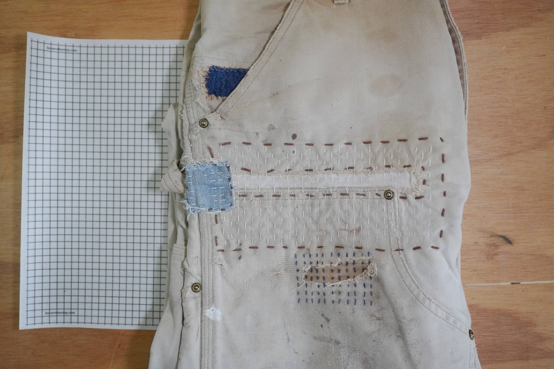 Worn beige vest with patches on a wooden surface next to graph paper