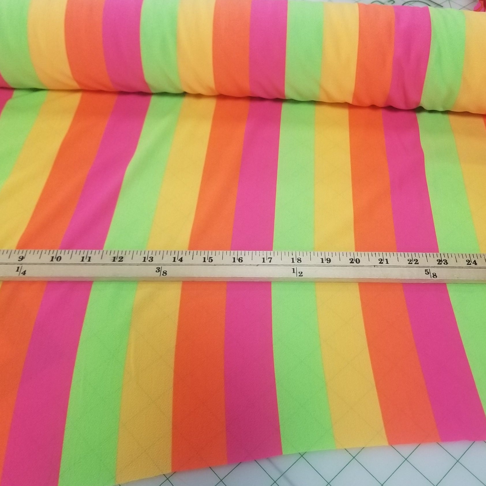 Colorful striped fabric with a ruler for scale on a cutting mat. LA Finch Fabrics Deadstock